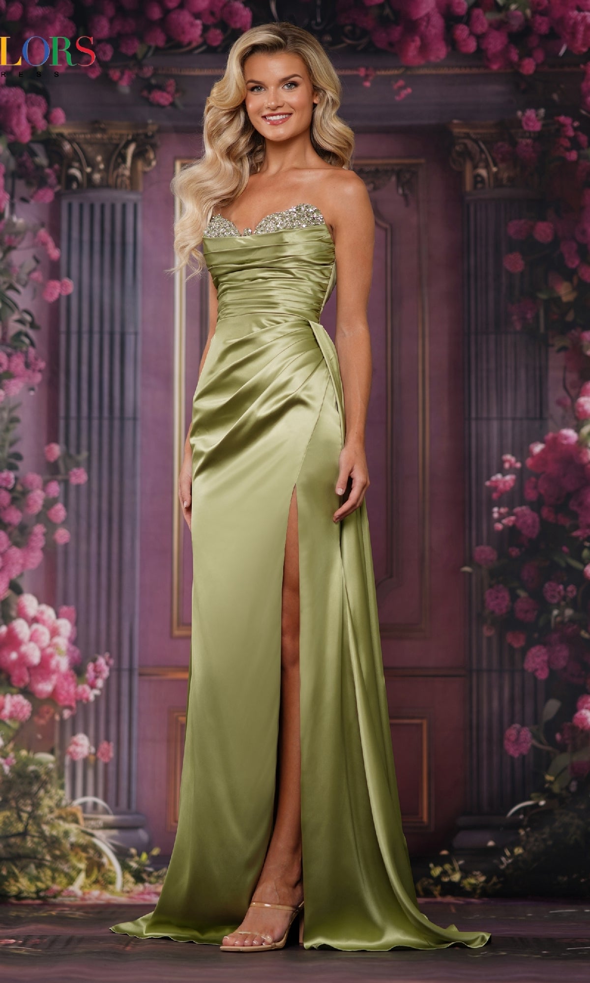 A woman wearing the Colors Dress 3854, a strapless satin long prom dress with an embellished sweetheart neckline and thigh-high slit, stands before a floral and column backdrop.